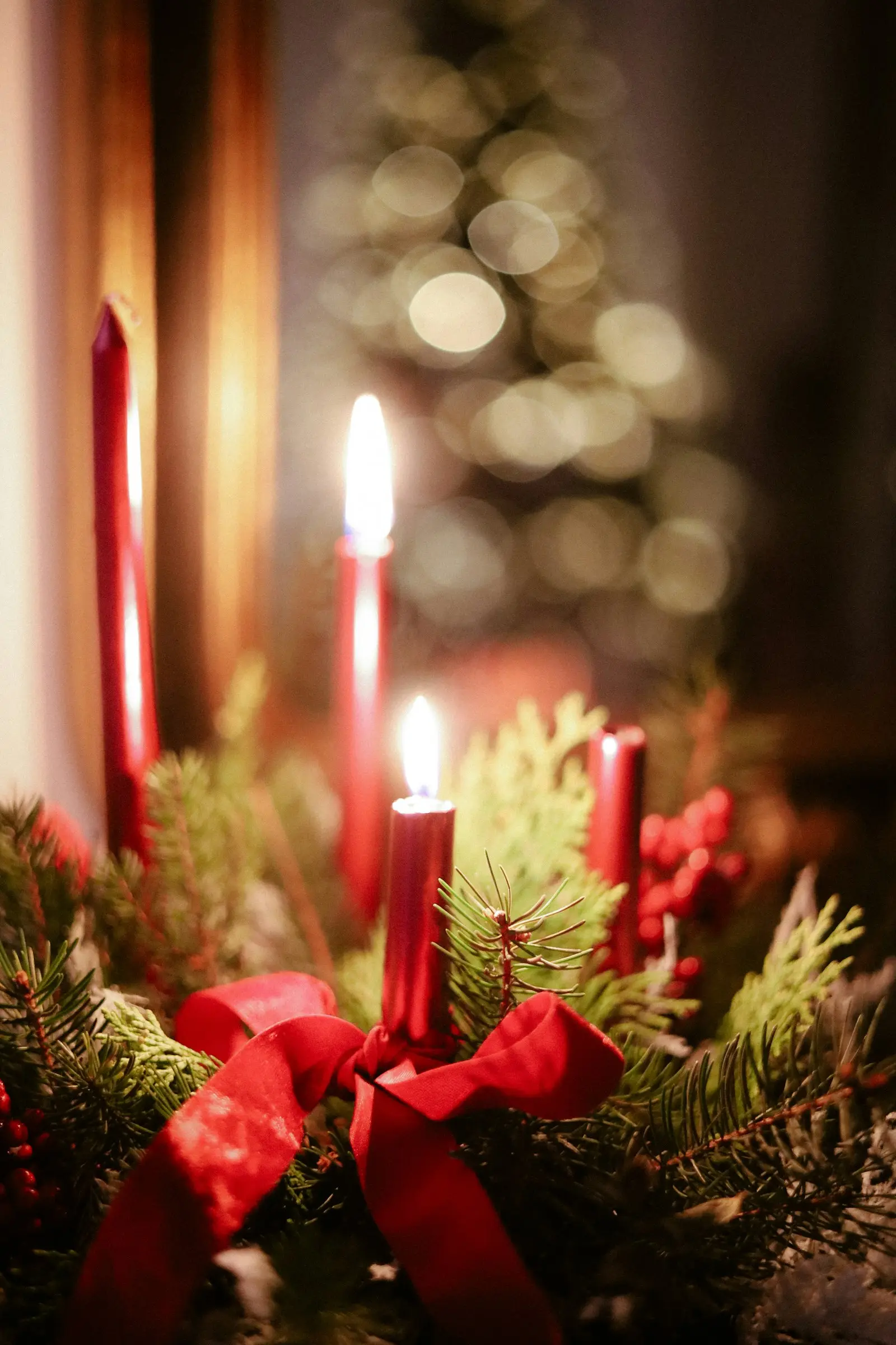 Couronne de l'Avent en sapin avec bougies rouges allumées et baies rouges