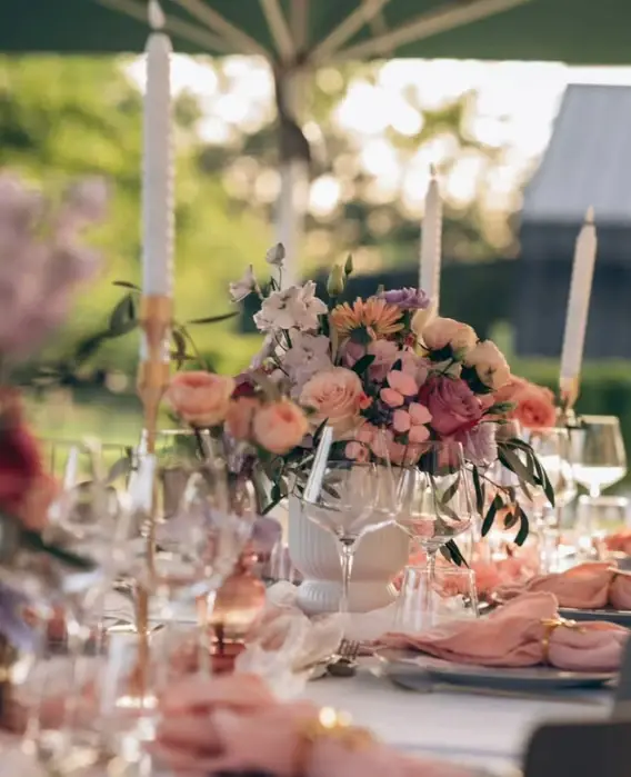 Table de réception en plein air dressée avec un bouquet champêtre de roses pêche et de fleurs roses, composé par Mily Fleurs